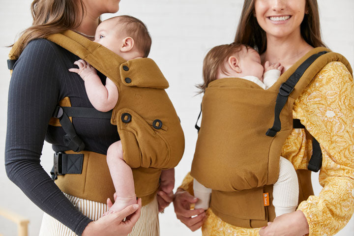 Zwei Mütter tragen ihre Kinder in den Tula Explore und Tula Free-to-Grow Babytragen