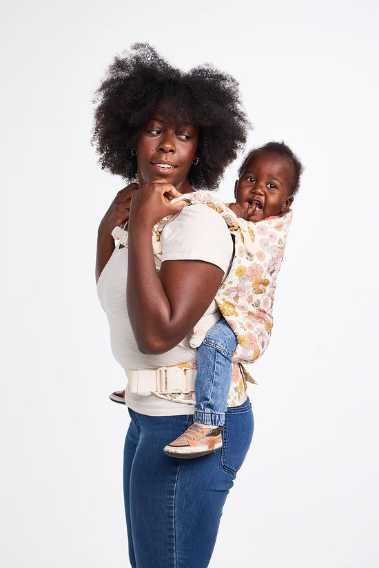 Une maman porte son enfant sur le dos à l'aide de son porte-bébé Toddler