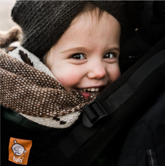 A closeup of a snuggled up child in a baby carrier from Tula.