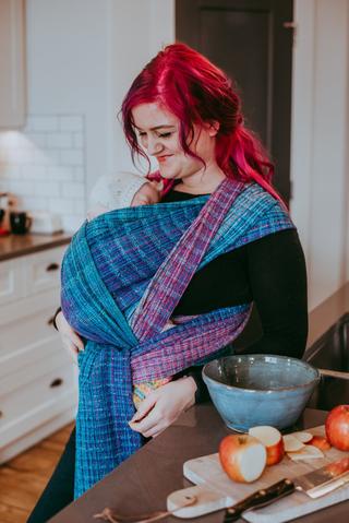 A mother carrying her sleeping child in a colourful Half Buckle Carrier.