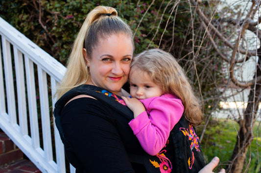 A caregiver smiling into the camera while carrying their child in a baby carrier.