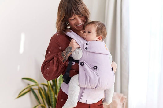A mother snuggling her child in a baby carrier