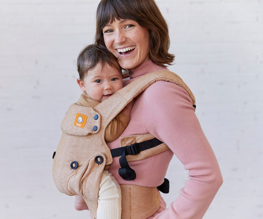 Happy parents gathered around their sleeping baby in a baby carrier.