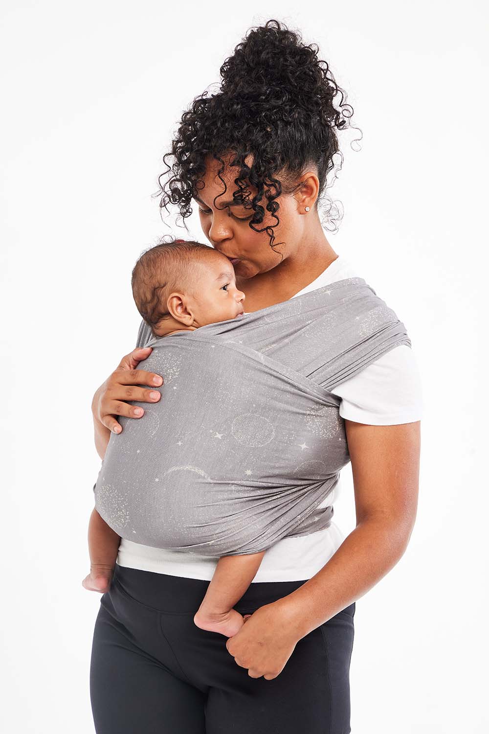 Mum kissing her baby's forhead wearing a Tula Stretchy Wrap Mystical