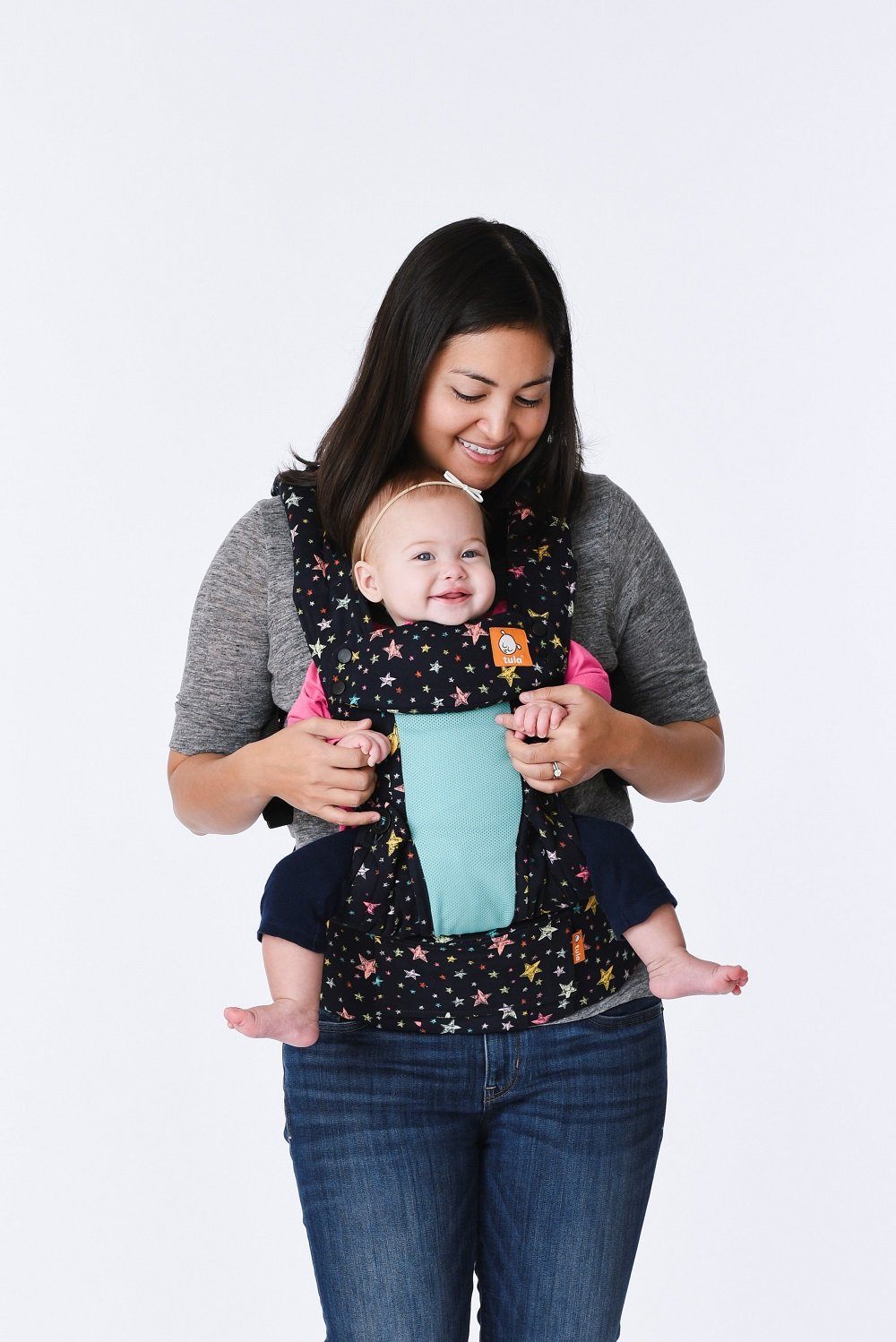 A baby who is smiling while sitting in the Explore Baby Carrier Coast Rainbow Stars.