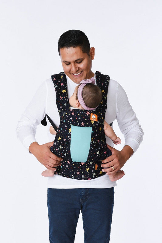 A baby looking at her caregiver while sitting in the Explore Baby Carrier Coast Rainbow Stars.