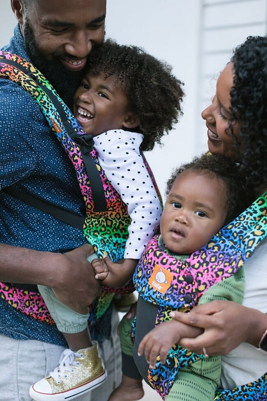 Smiley toddler being worn in a rainbow coloured hip healthy carrier