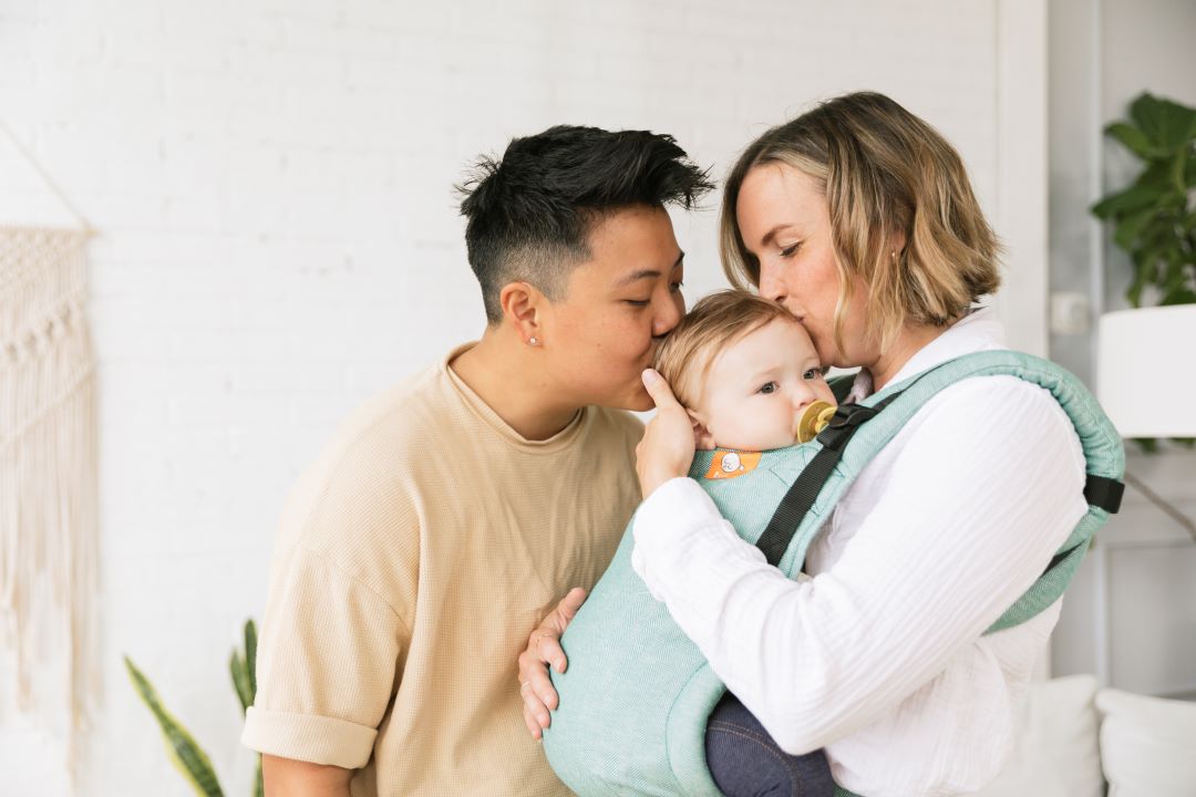 two mums kissing baby in a linen baby carrier from birth