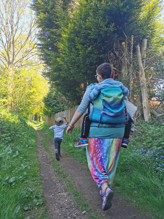 Eine Mutter mit einer Preschool Trage  von Tula und ihrem Kind, das vor ihr herläuft.