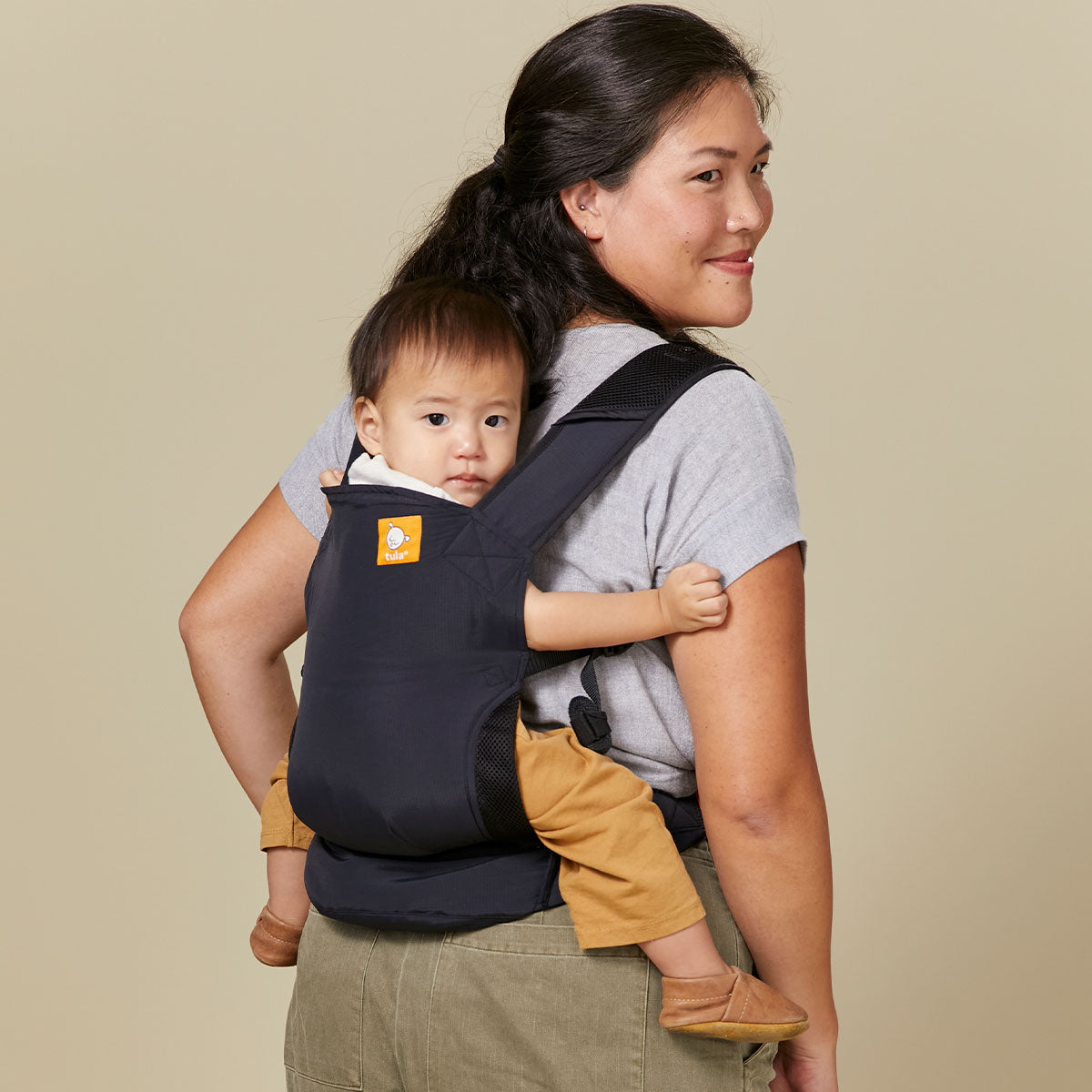 Eine Mutter trägt ihr Kind auf dem Rücken in der Tula Lite Babytrage