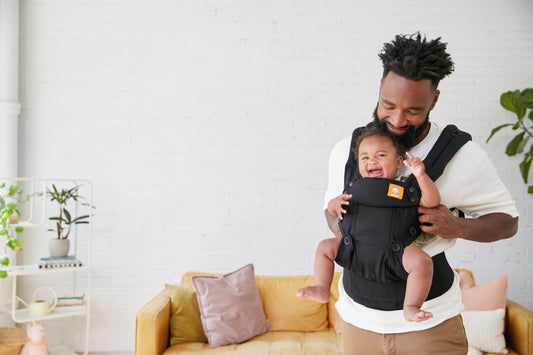 Un padre lleva a su bebé en una mochila portabebé Tula en posición de porteo frontal.
