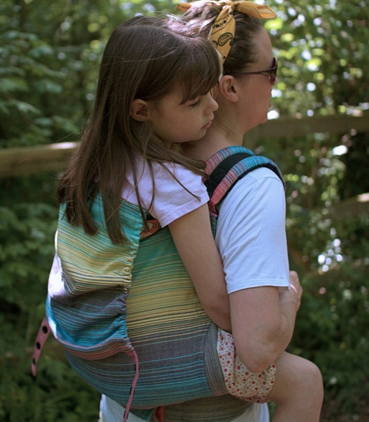 Una madre lleva a su hija en un colorido portabebés de Tula.