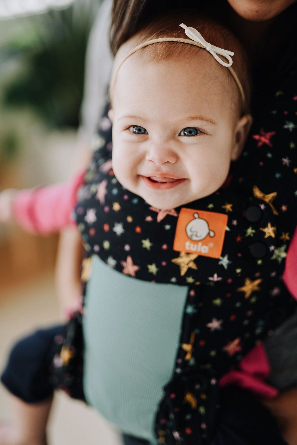 Vauva hymyilee kameraan istuessaan Explore vauvan kantokopassa Coast Rainbow Stars.