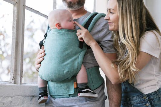 Isä pitää vauvaa vastasyntyneelle tarkoitetussa kantokopassa sisäänpäin suuntautuvassa kantoasennossa.