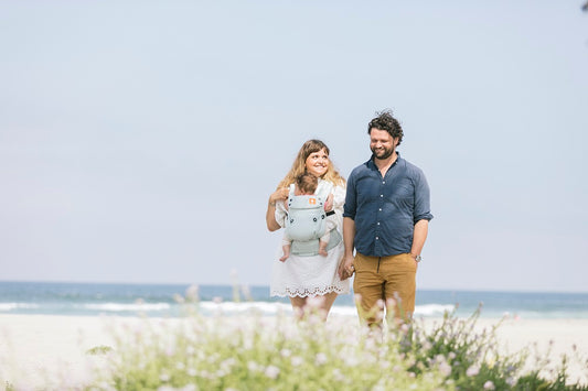 Parents portant leur enfant dans un porte-bébé Tula lors d'une promenade à la plage.