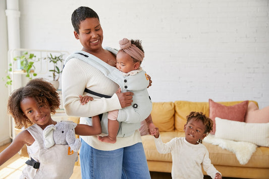 Une mère porte son bébé dans un porte-bébé Tula. Ses autres enfants sont autour d'elle.