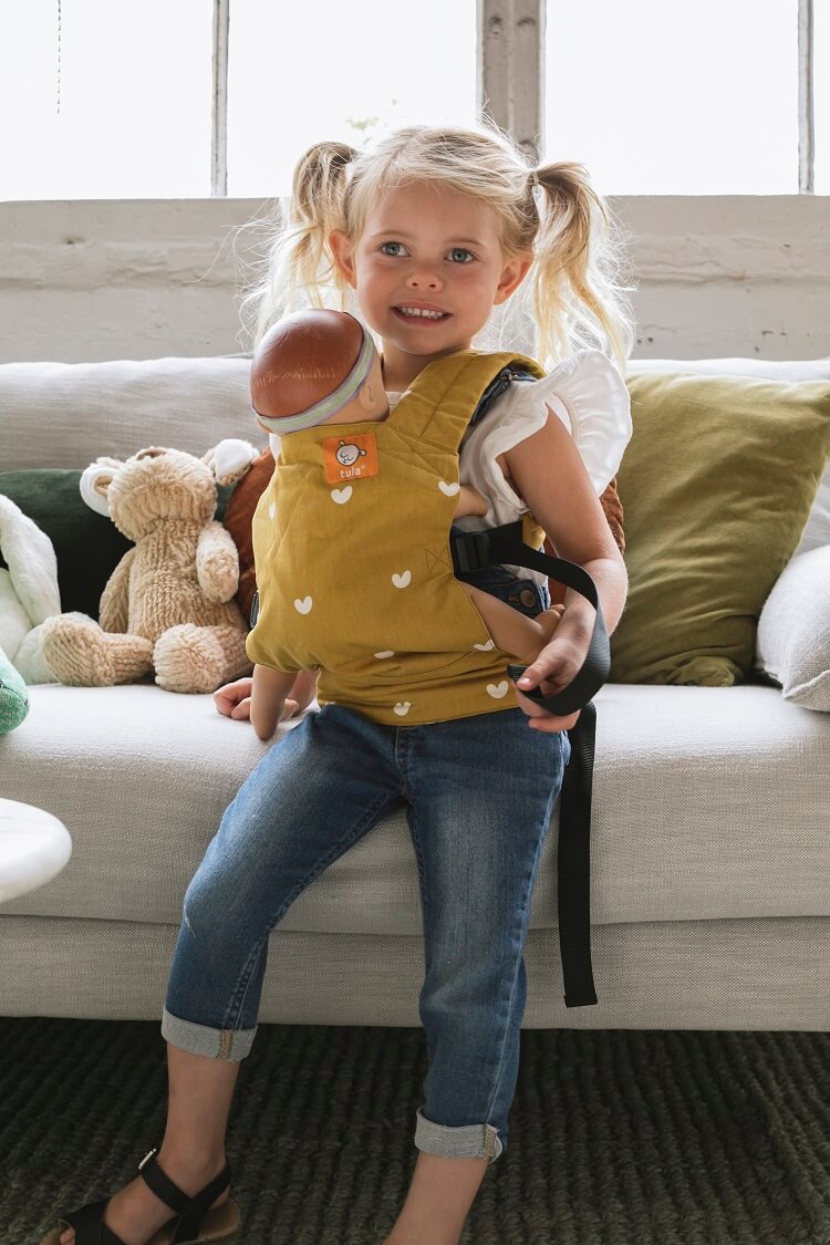 Une petite fille souriante transportant son porte-poupon Mini.