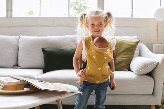 Une petite fille souriante transportant son porte-poupon Mini.