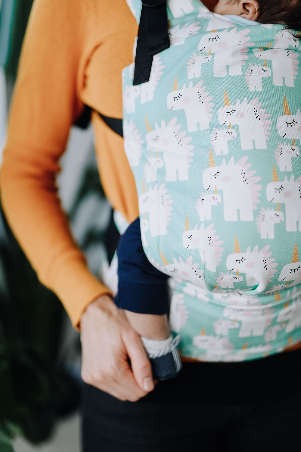 Un primo piano di una babysitter nell'ergonomica Tula Free-to-Grow Marsupio  Unisaurus in posizione di trasporto anteriore.