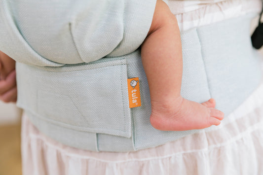 Close-up van een linnen draagzak waar een baby in zit.
