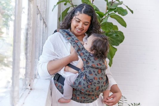 Een moeder ademt haar kind in een babydraagzak met hulp van een andere vrouw.