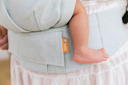 Grande plano de um porta-bebés de linho onde está sentado um bebé.