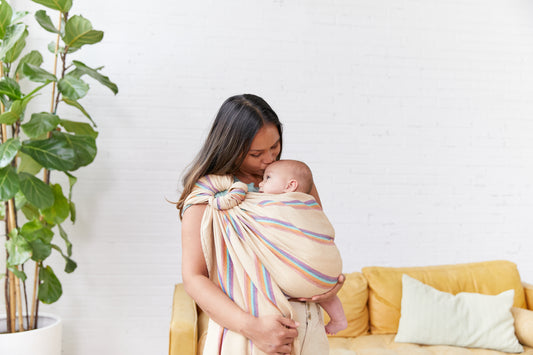 Uma mãe beija o seu filho na testa enquanto utiliza uma funda Tula Ring Sling.