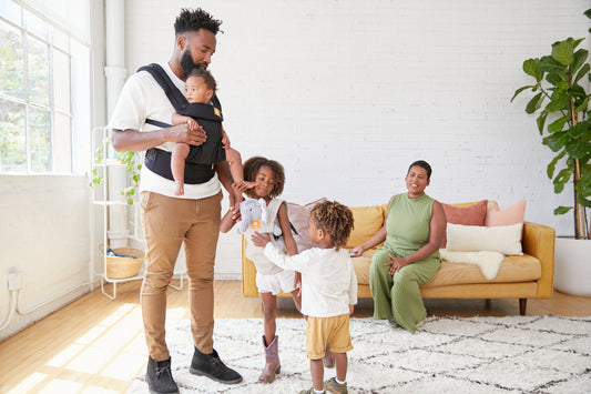 Uma família de cinco pessoas que utiliza o porta-bebé Tula Coast e o porta-brinquedos Tula Mini.