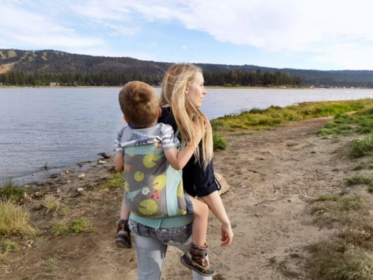 Uma mãe carrega o seu filho às costas enquanto exploram a natureza.