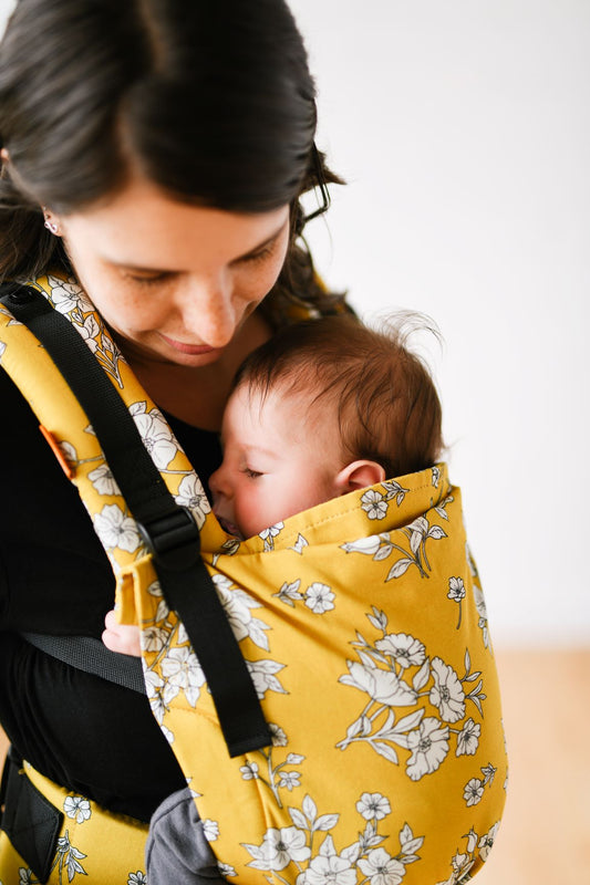 Uma mãe que transporta o seu filho adormecido em posição de transporte frontal.