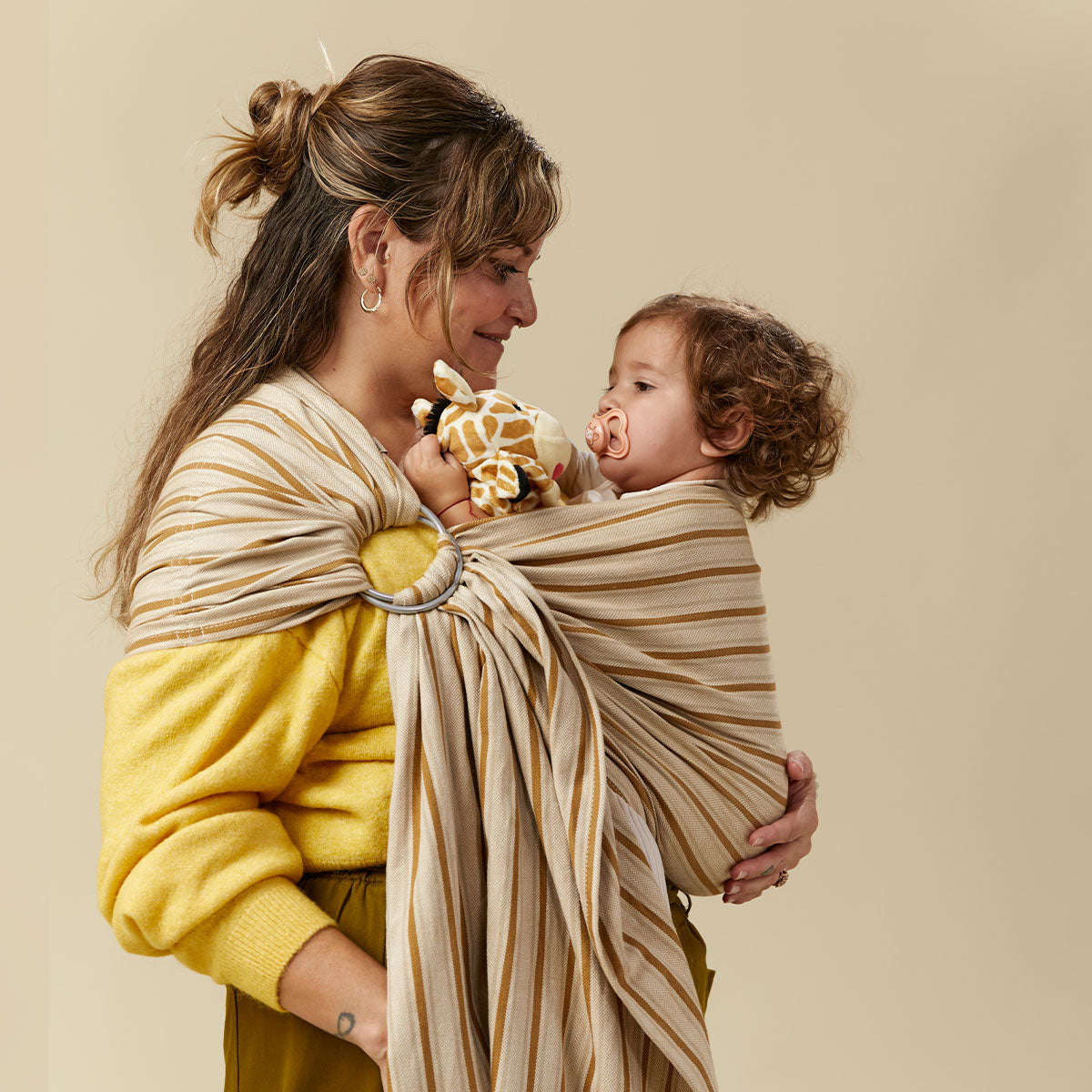 uma mãe a transportar a sua filha adormecida numa Tula Ring Sling Latte